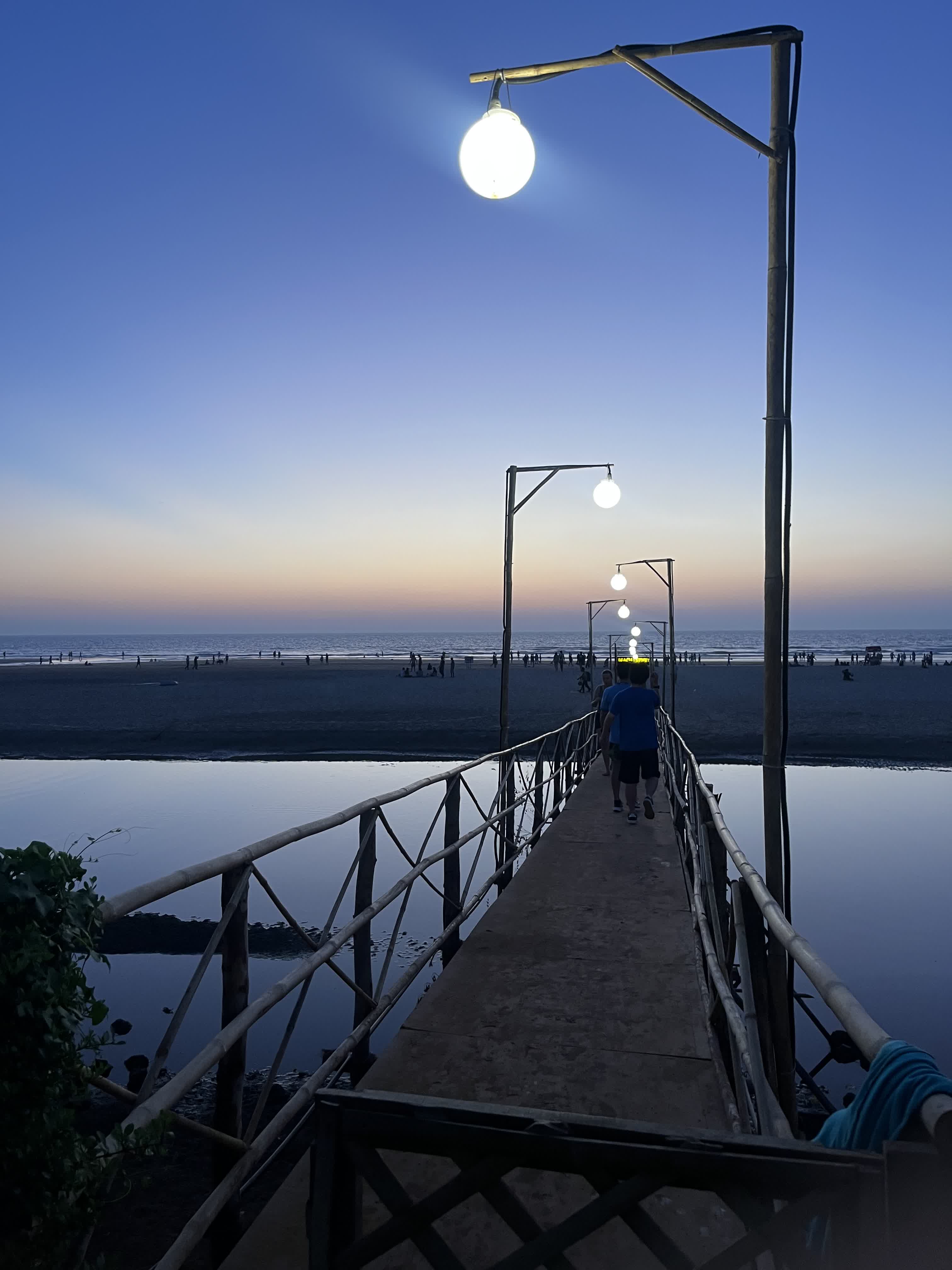 A wooden jetty leading to the beach at dusk with lit lamps