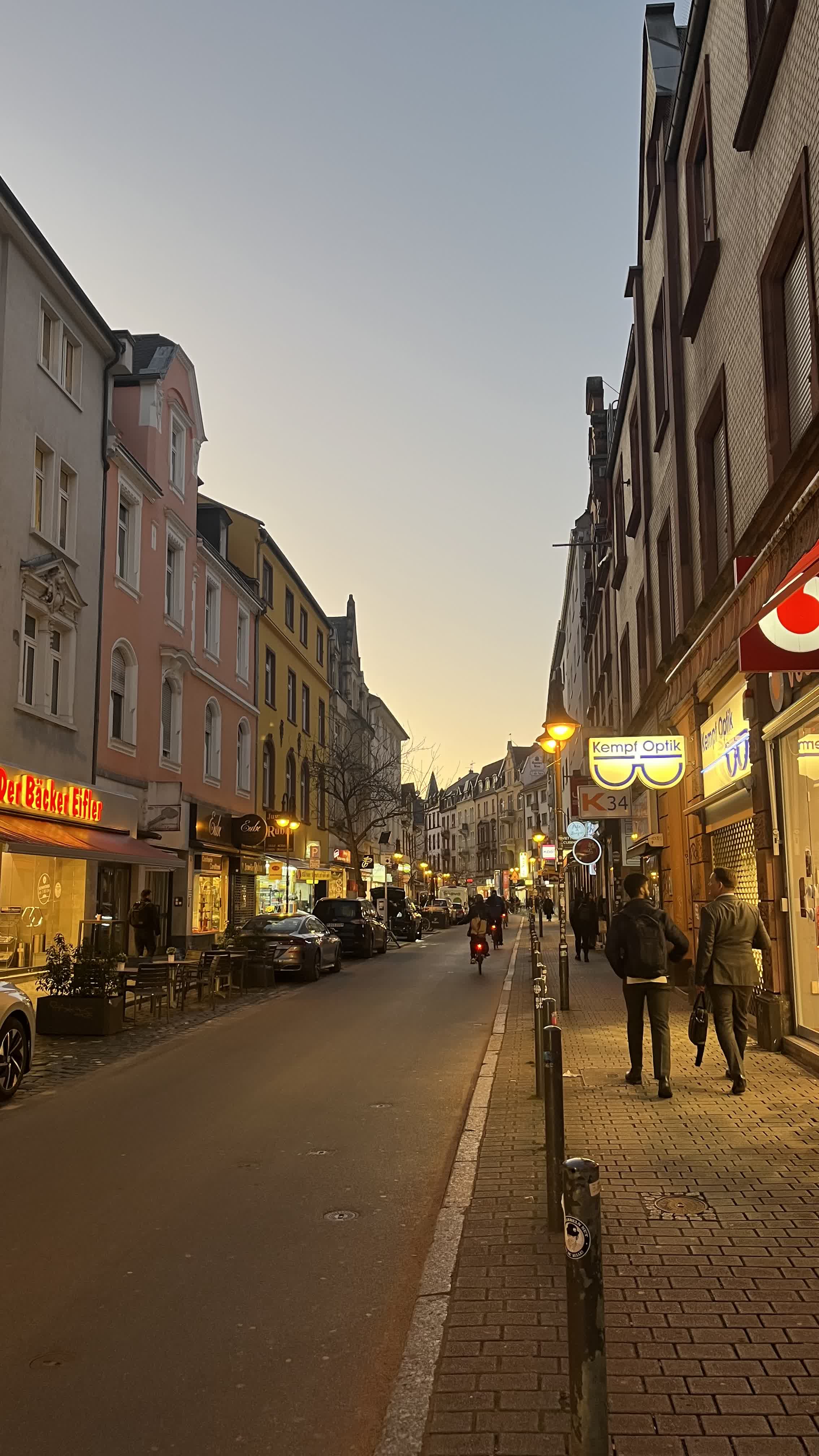 A Frankfurt street at dusk with pastel buildings and shop signs