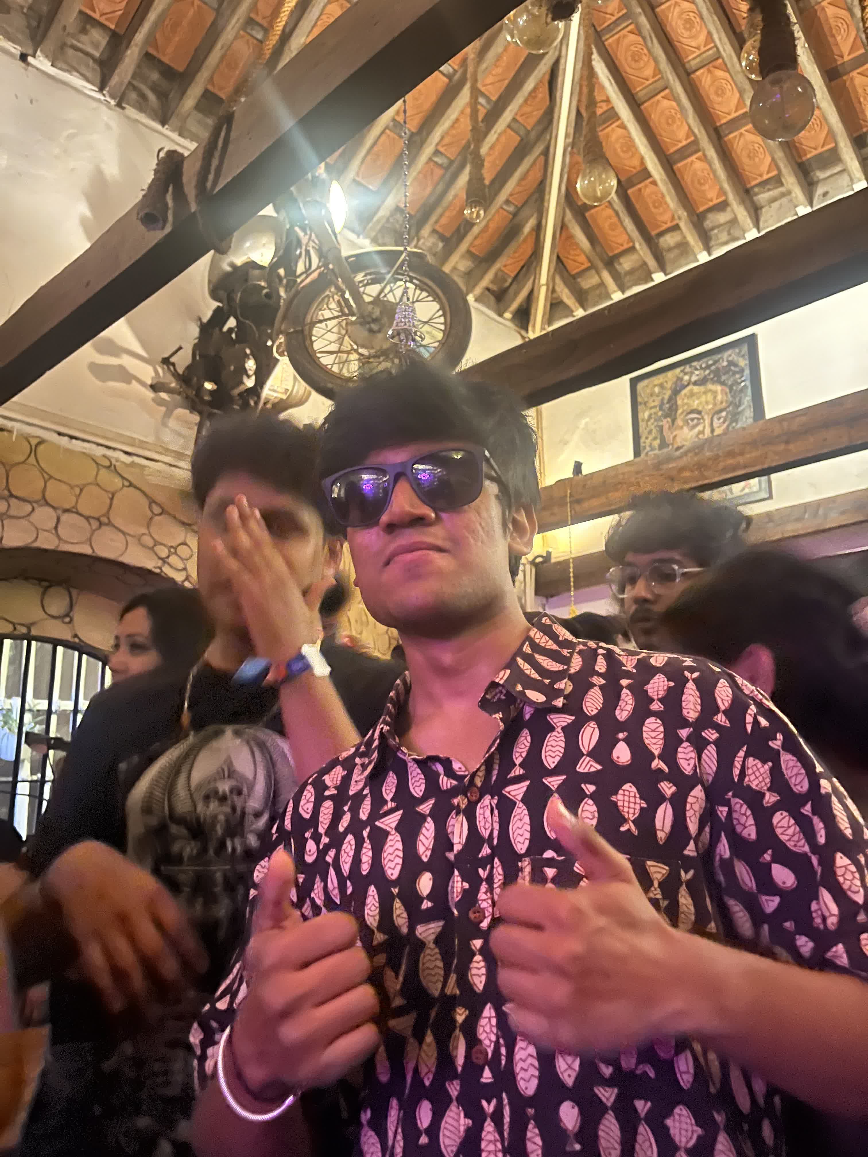 In a printed shirt and sunglasses at a Goan beach shack with a motorbike on the ceiling