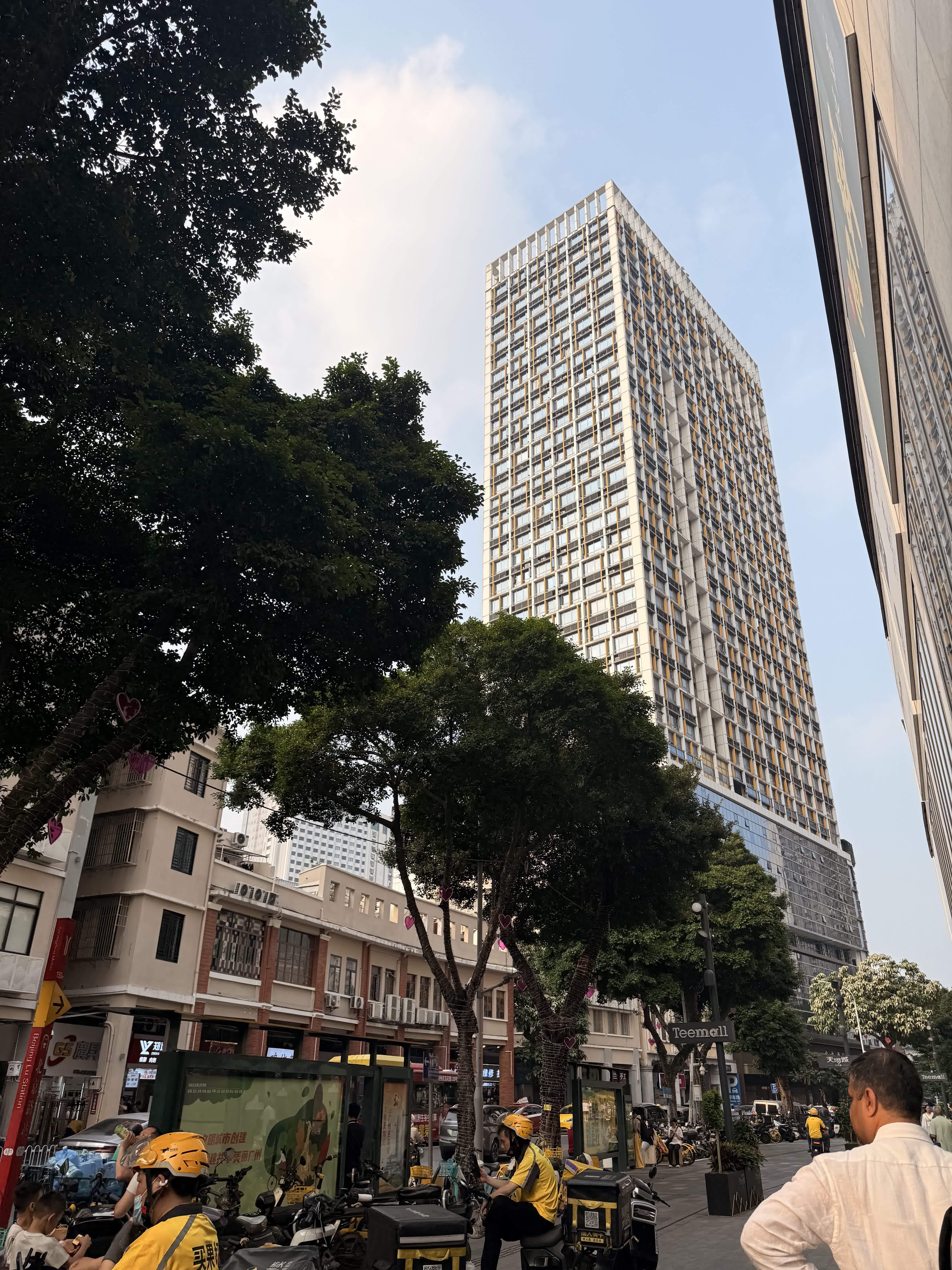 A tower rising over an older Guangzhou street with delivery riders below