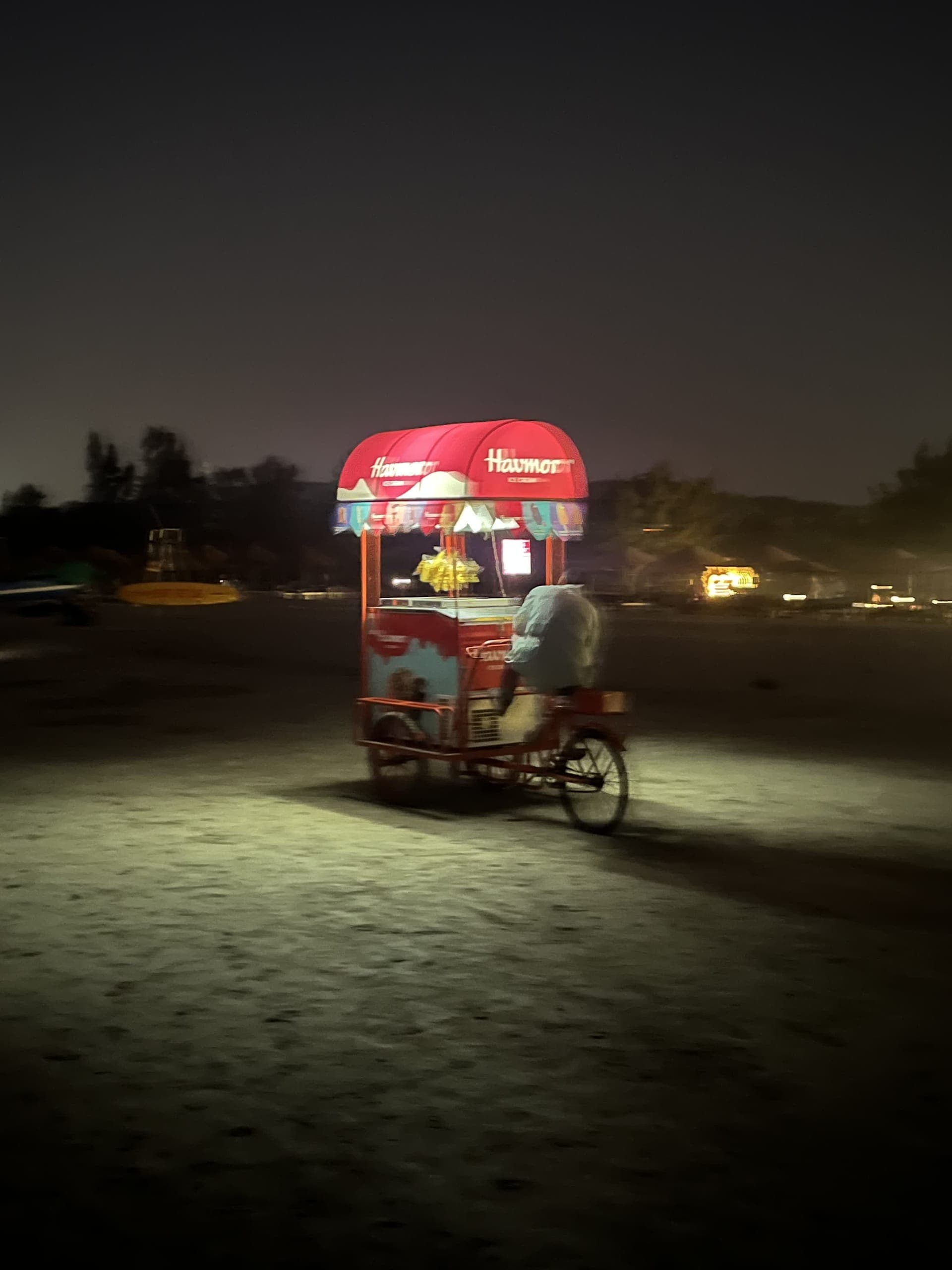 A lit Havmor ice-cream cart on the dark beach at night