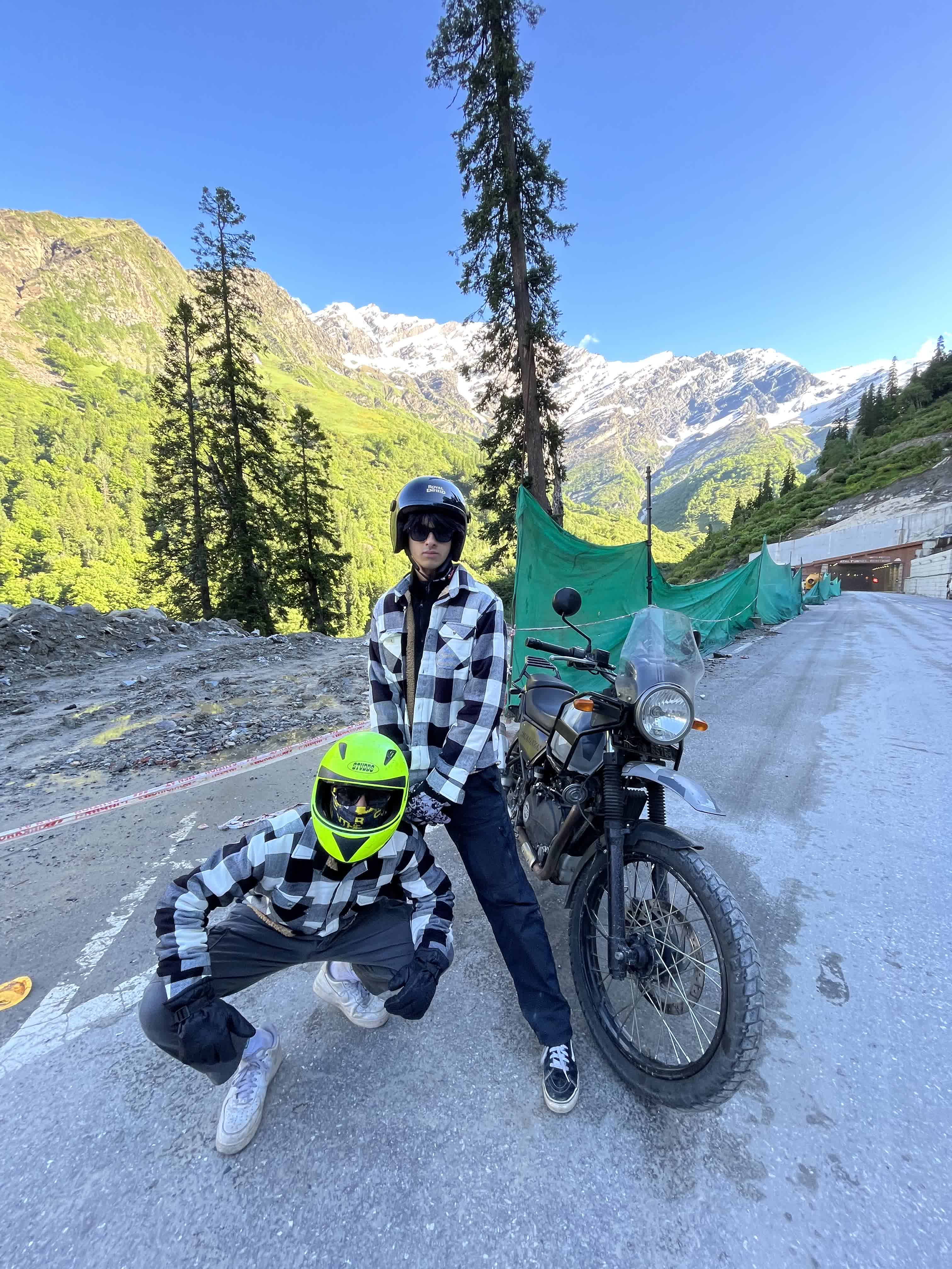 Two of us with a Royal Enfield Himalayan on a mountain road under snow-capped peaks