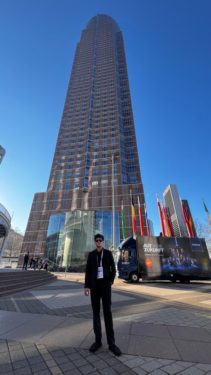 Standing in a suit with an exhibitor badge in front of the Messeturm tower and international flags