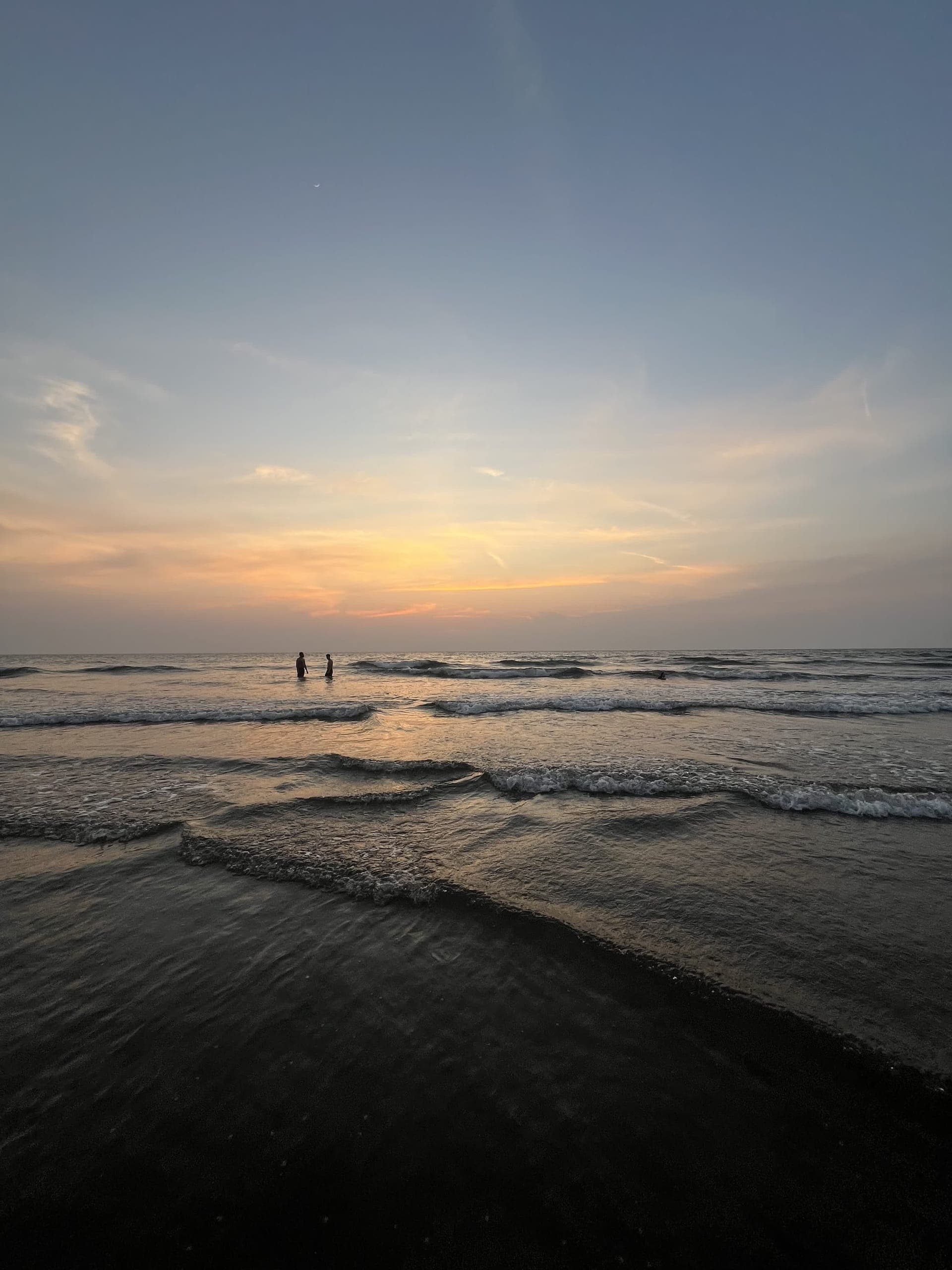 Two silhouettes wading into the sea at sunset