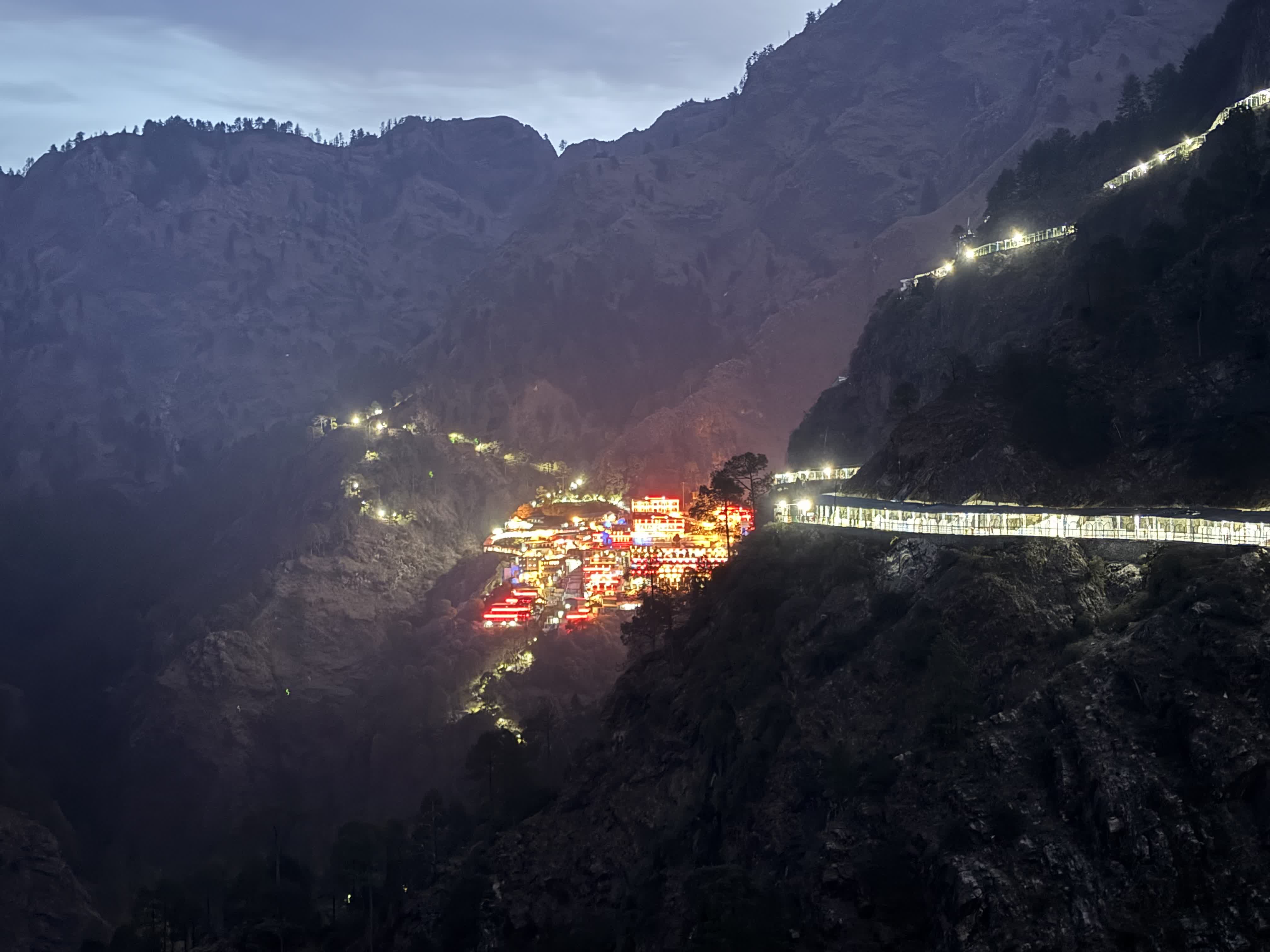 The Vaishno Devi shrine lit up red and gold on the mountainside at night